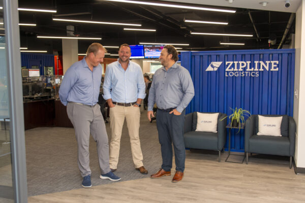 three businessmen talking in the open concept office space with the zipline logo visible on the right