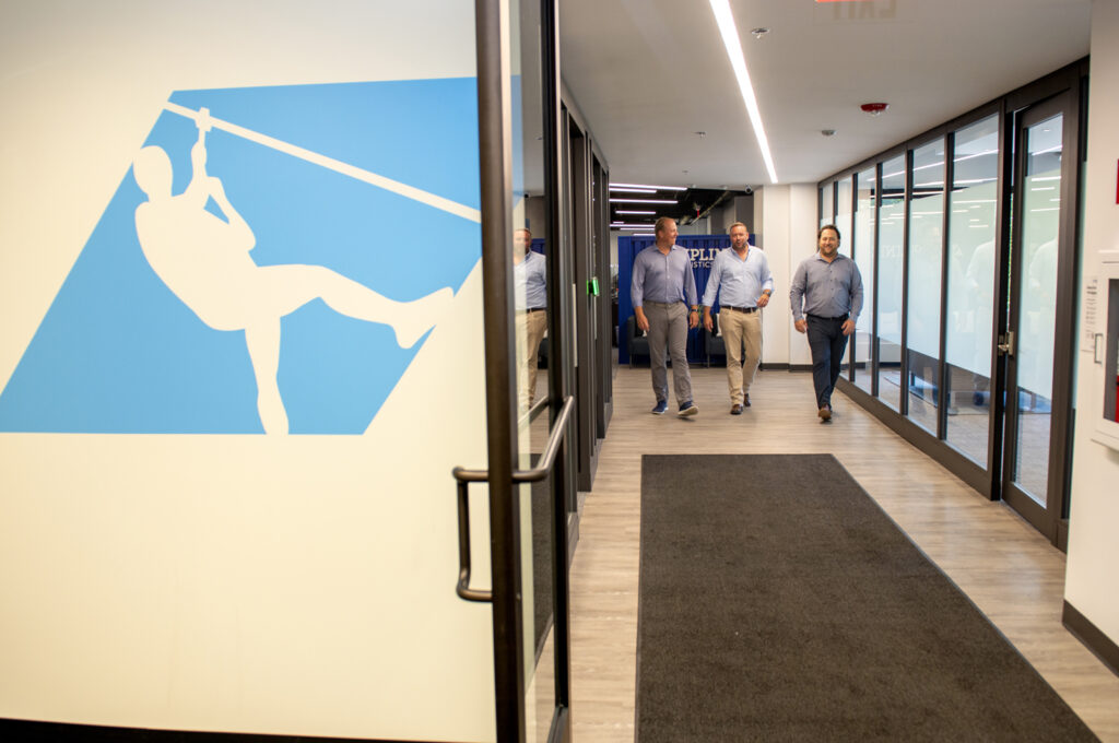 Three business partners walking down hall with zipline logo visible on the wall